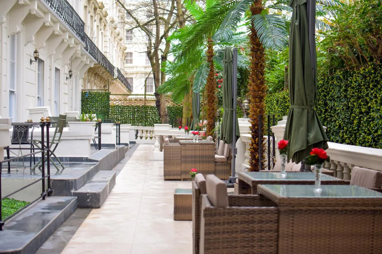 a patio with tables and chairs and palm trees at Pembridge Palace Hotel in London