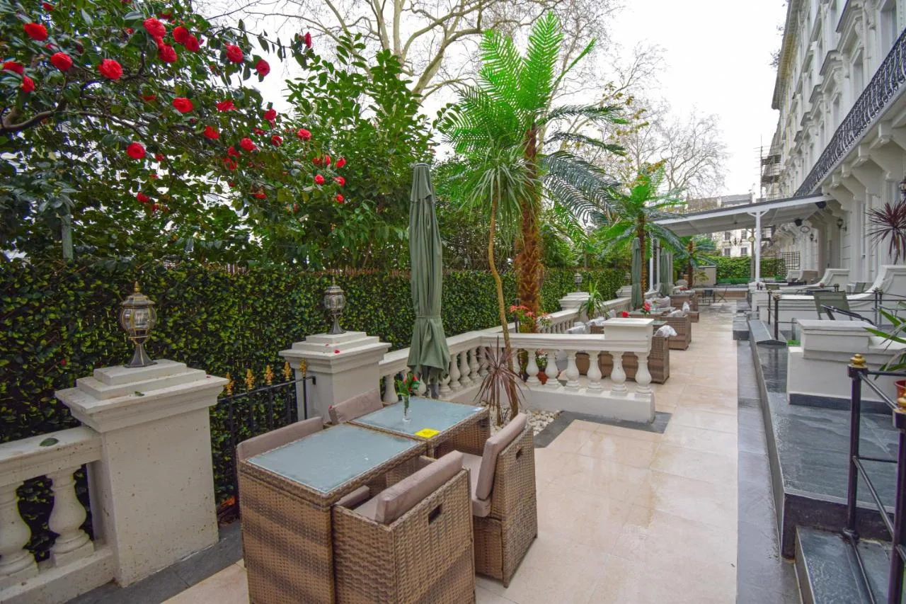 a patio with chairs and a fence and flowers at Pembridge Palace Hotel in London