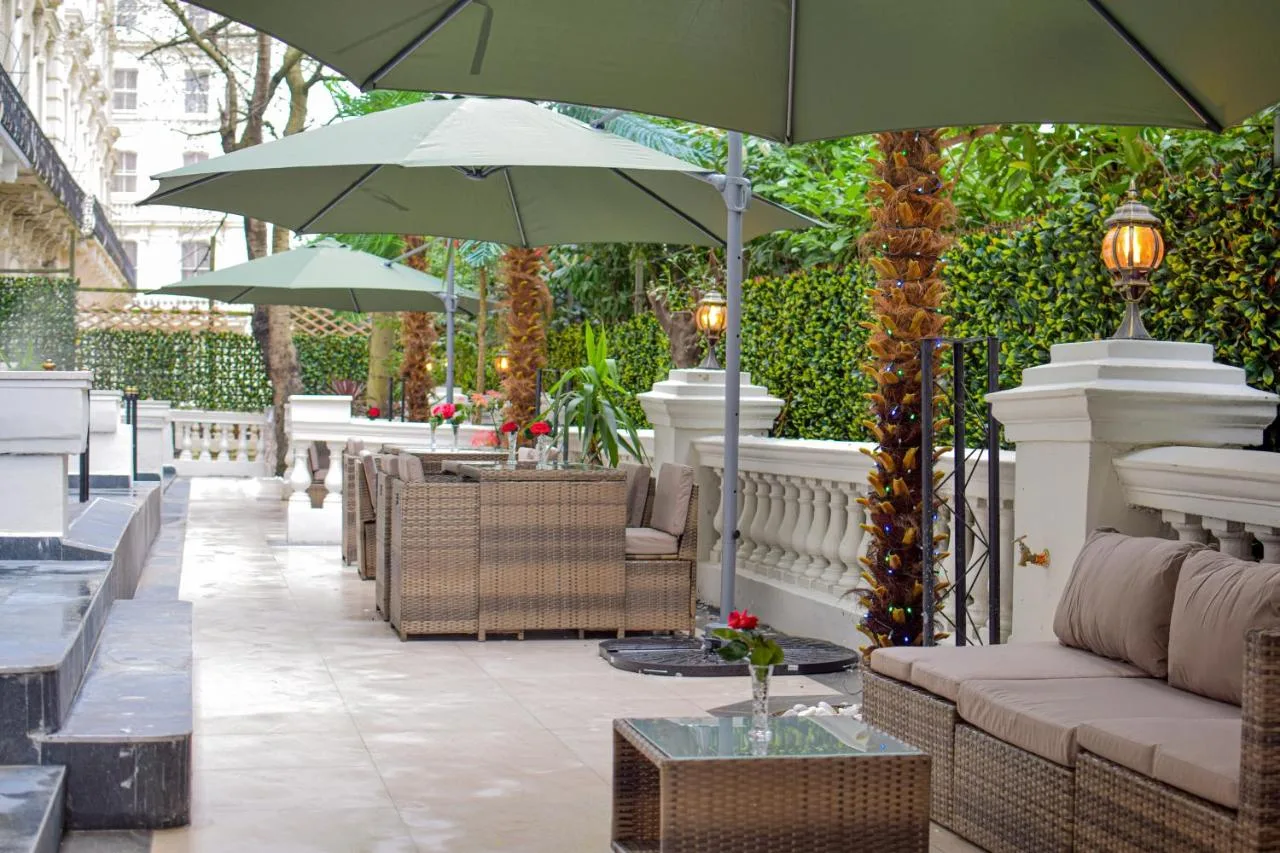 a patio with couches and tables and umbrellas at Pembridge Palace Hotel in London